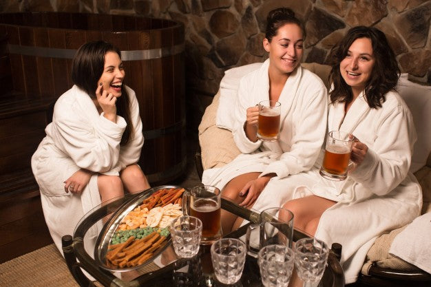 women enjoying cold beer while sitting outside a sauna and wearing a bathrobe 