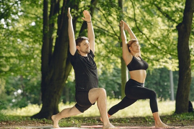 Image alt text: A young healthy couple practicing yoga in the park in matching athletic wear 